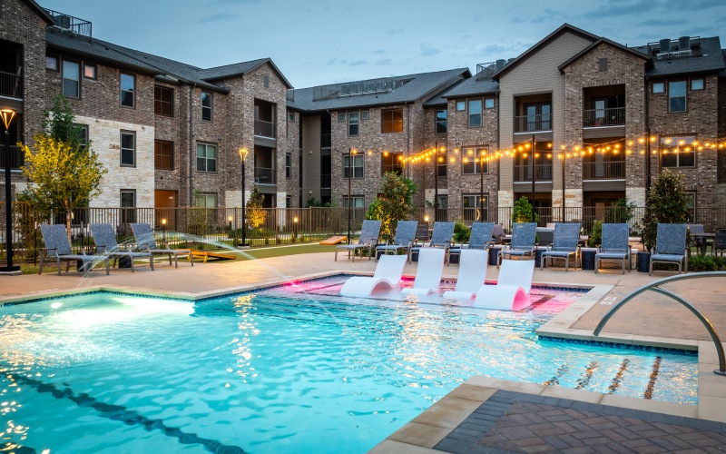 A pool with tanning deck and white chairs