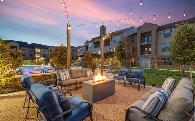 a patio with a fire pit and chairs and a building with a sunset