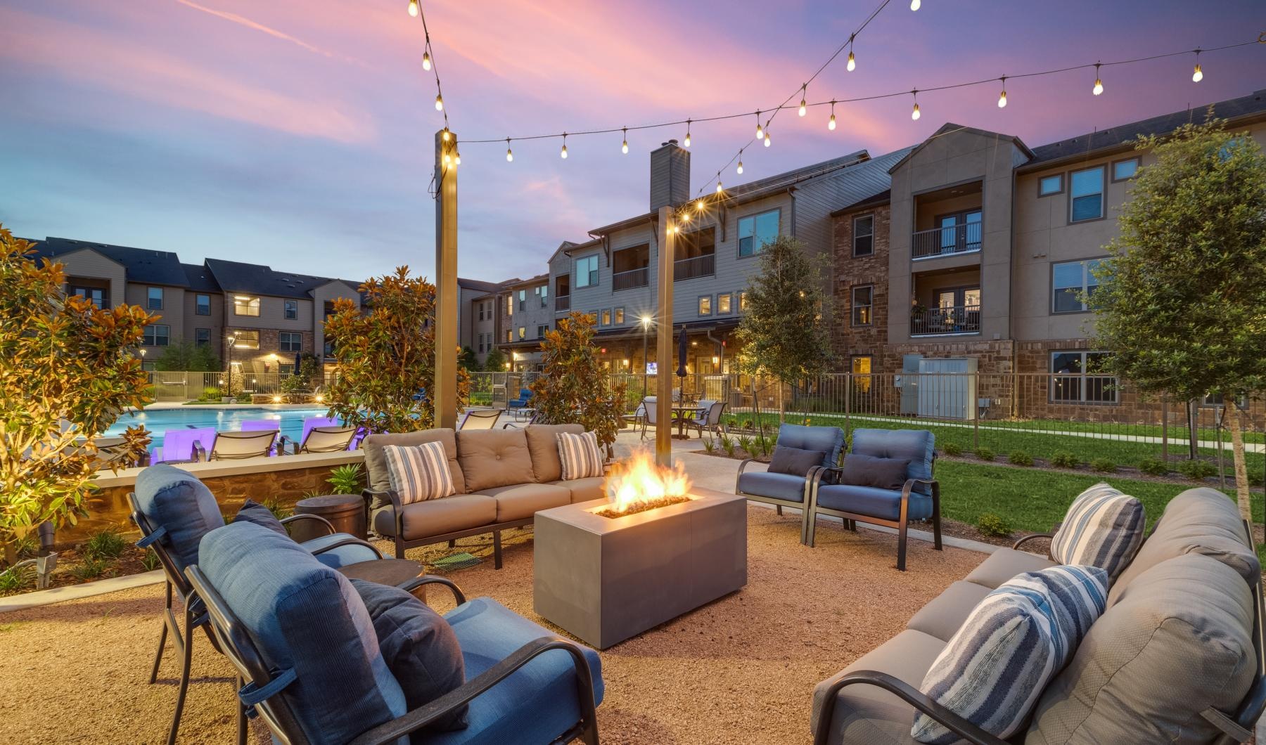 a patio with a fire pit and chairs and a building with a sunset