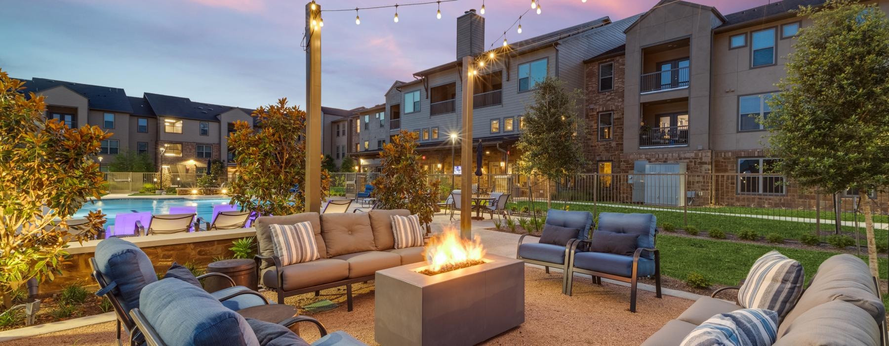 a patio with a fire pit and chairs and a building with a sunset